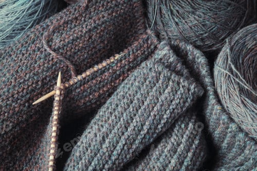 Preview: Unfinished gray scarf, knitting needles and a round skein of wool.