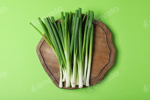 Preview: Wooden board with fresh spring onion on green background