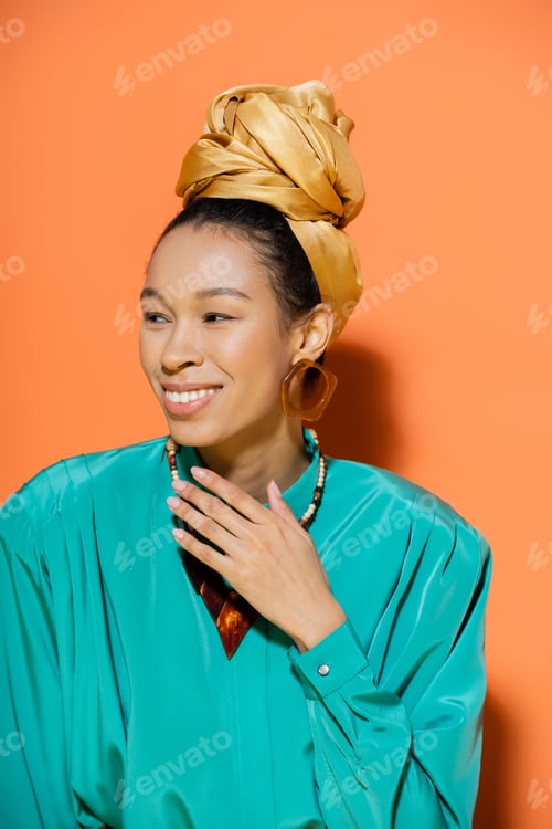 Preview: Portrait of cheerful african american model in headscarf looking away on orange background