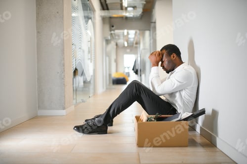 Preview: Portrait shot of African American sad businessman in suit and tie sitting with box of stuff.