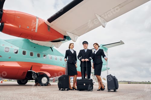 Preview: Pilot in uniform and two stewardess is outdoors near plane
