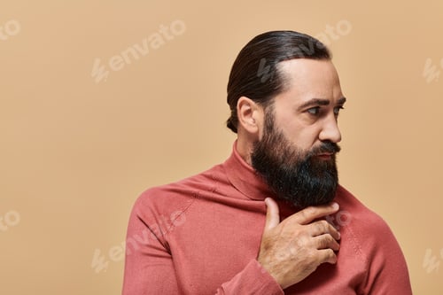 Preview: portrait of handsome man with beard posing in turtleneck jumper on beige background, serious