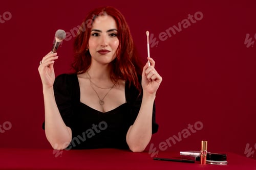 Preview: Woman looking at camera while holding makeup brushes standing against an isolated background.