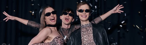 Preview: Group of cheerful and trendy homosexual friends in party outfits and sunglasses standing under