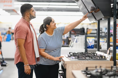 Preview: Couple of young customers looking at buildin cookers in domestic appliances shop