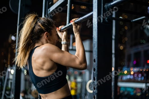 Preview: Woman exercises at night using a pull-up bar in an urban gym setting with lights in the background
