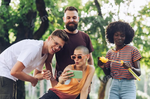 Preview: Multiracial friends are standing in a park and taking selfies.