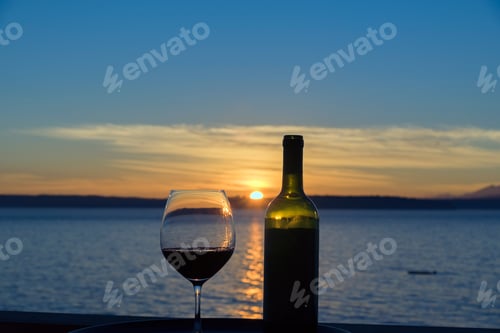 Preview: Red wine in glass at sunset outside by the sea.