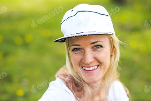 Preview: Portrait of a beautiful woman in a white baseball cap on the background of the park in spring