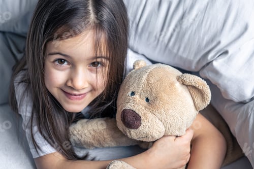Preview: Little cute girl in bed with a teddy bear early in the morning.