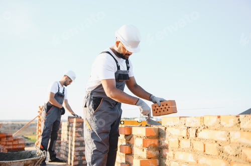 Preview: A team of Indian construction workers in overalls and hard hats are building a brick wall