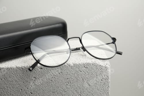 Preview: Stylish glasses and case on stone surface against light grey background, closeup