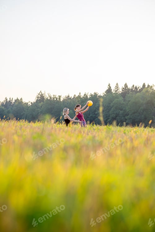 Preview: Low angle view of pilates trainer and trainee working out with a yellow ball outside in nature