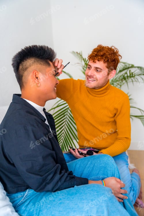 Preview: Beautiful gay couple putting on makeup and having fun being romantic indoors at home, lgbt concept