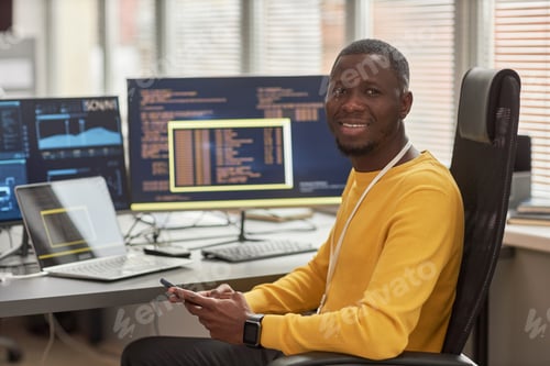 Preview: Smiling black man looking at camera at workplace in software development