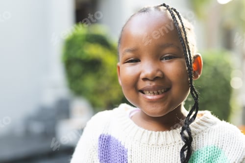 Preview: Portrait of happy african american girl with braids standing outside house