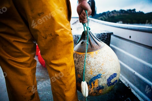 Preview: A fisherman in yellow waders on his boat moving a large fishing float.