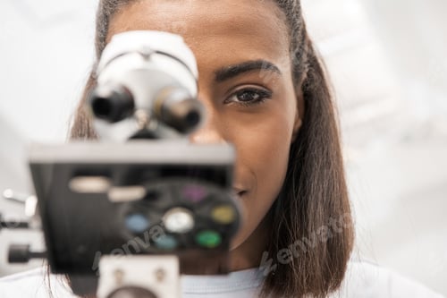 Preview: partial view of woman scientist looking through microscope on reagents in laboratory
