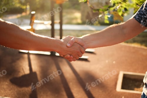 Preview: Male handshake in the street against the background of the sports ground.