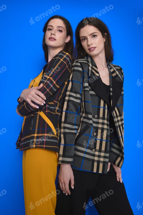 Preview: Twin sisters showcase stylish outfits against a vibrant blue backdrop during a fashion shoot