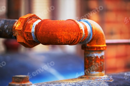 Preview: Rusty metal pipe against a blurred brick wall background.