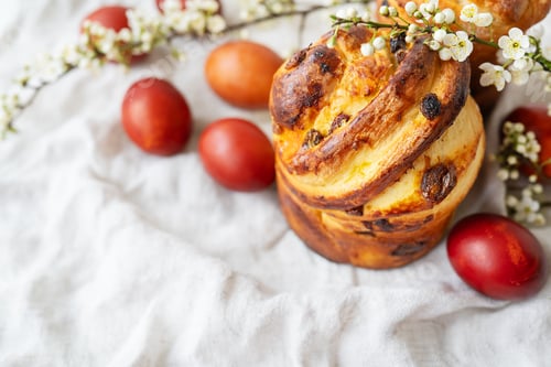 Preview: A traditional Easter bread with painted eggs and blossoms on a textured fabric. Festive, colorful