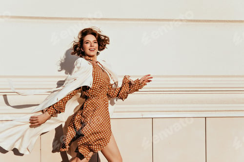 Preview: Gorgeous happy girl in brown dress running down the street. Outdoor portrait of beautiful caucasian