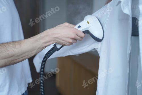 Preview: Cropped shot of man using electric garment steamer while steaming while classic shirt at home