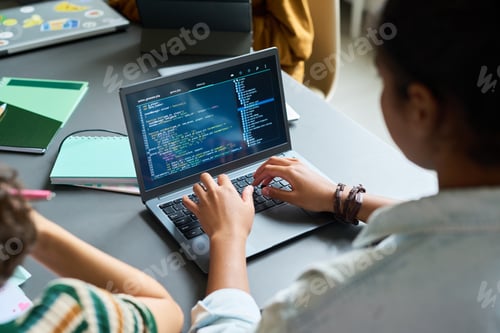 Preview: Young Adult Woman of Color Writing Code on Laptop Computer in Office Setting
