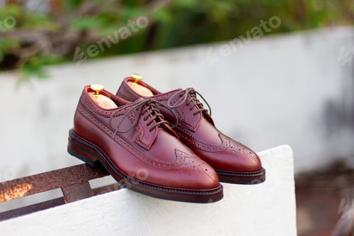 Preview: Closeup of a pair of a men's brown leather shoes against a blurred wall background