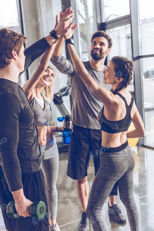 Preview: Happy young athletic people in sportswear giving high five in gym