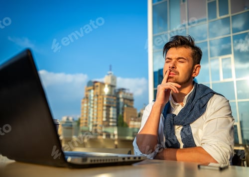 Preview: Thoughtful businessman working on laptop outdoors.