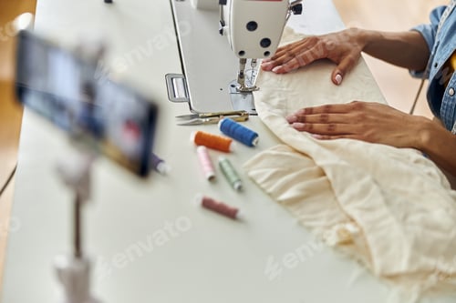 Preview: African-American dressmaker sews white fabric with new machine at table in studio