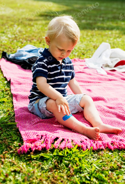 Preview: Full length of boy with bandage on leg sitting on picnic blanket