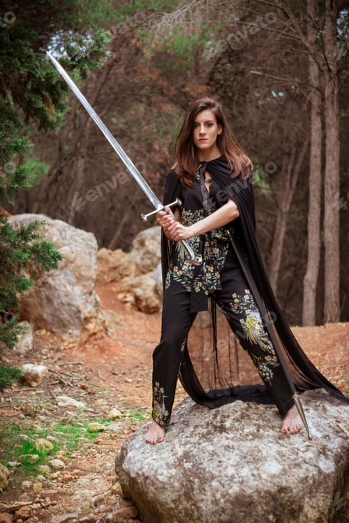 Preview: Vertical shot of a powerful young female with a sword posing in a forest