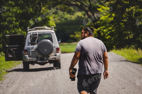 Preview: Back view of anonymous male traveler in casual clothes walking towards SUV car parked on road