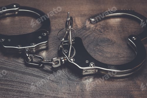 Preview: handcuffs and keys on brown wooden table background