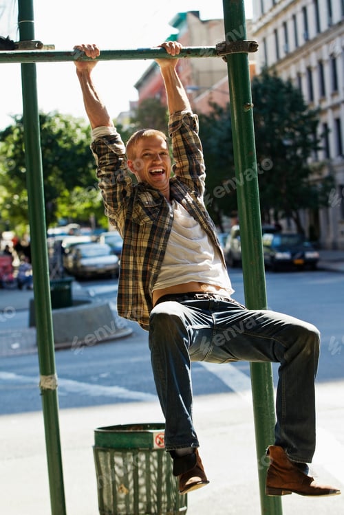 Preview: Man having fun hanging from a city playground bar