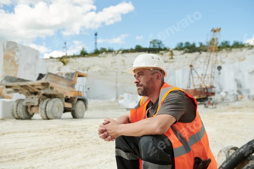 Preview: Tired worker of marble quarry sitting in front of camera by workplace