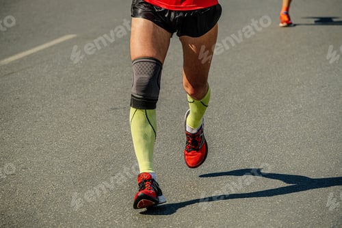 Preview: close-up legs male runner in compression socks and knee pads running marathon race