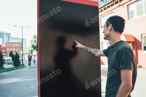 Preview: Cheerful young man pointing on blank billboard in street
