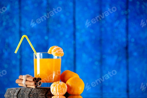 Preview: Front view of delicious fresh tangerine juice served with tube and cinnamon limes on wooden board on