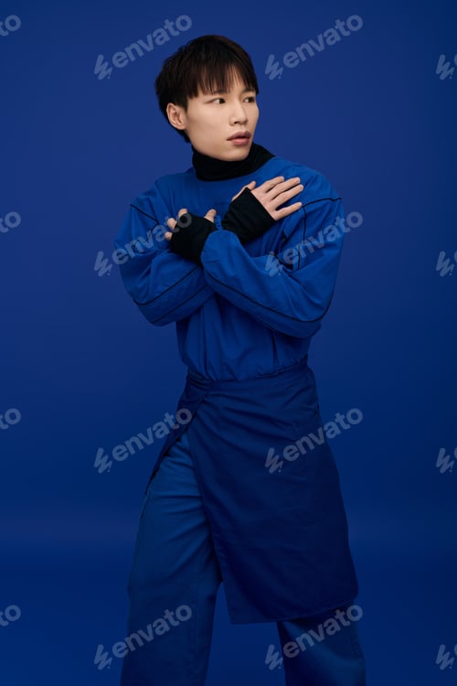 Preview: Striking young asian man poses in vibrant blue attire against a matching backdrop