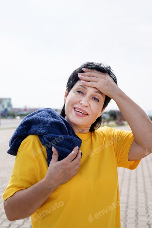 Preview: Smiling senior woman wiping out sweat after hard workout outdoors in the park