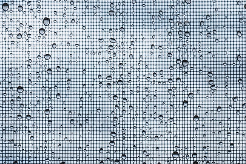 Preview: water drops on glass window with mosquito net against gray sky