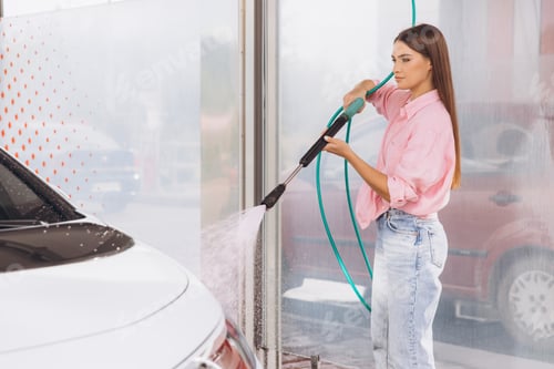 Preview: Young Woman Using Pressure Washer To Clean Car