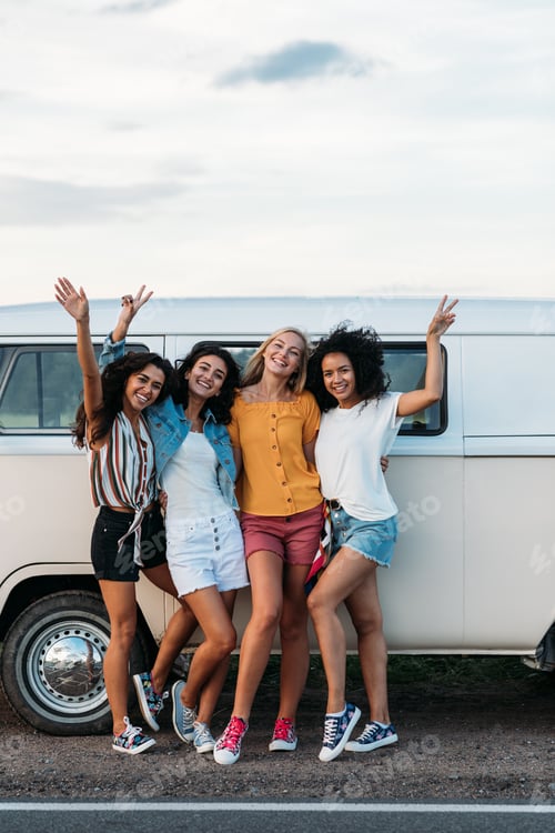 Preview: Four female friends in casuals standing at minivan on road raised hands up
