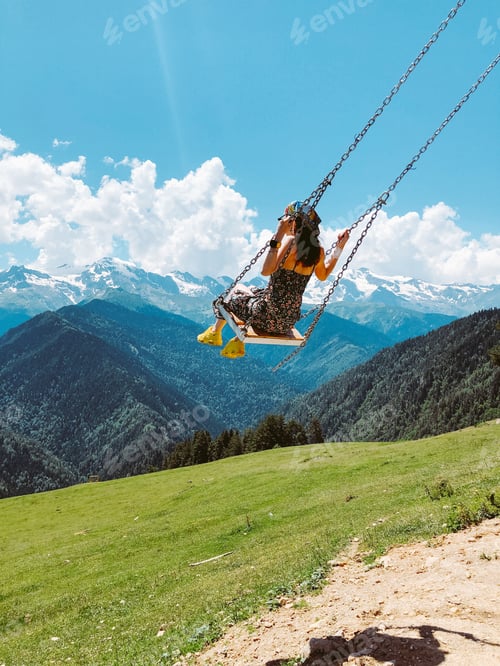 Preview: young woman rides on a swing in the mountains in summer