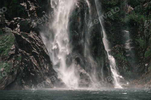 Preview: cascading water pouring down onto the calm calm blue lake waters in a greenery and nature setting
