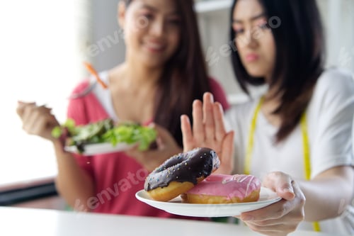 Preview: Two young Asian girls rejecting junk or unhealthy food such as donuts by pushing donut dish